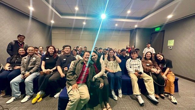 Group photo of attendees seated in a meeting room, smiling at the camera