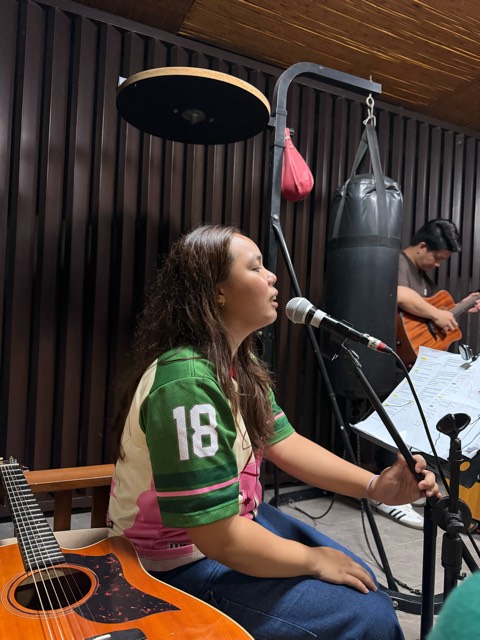 A young woman singing into a microphone during worship, a guitarist behind her