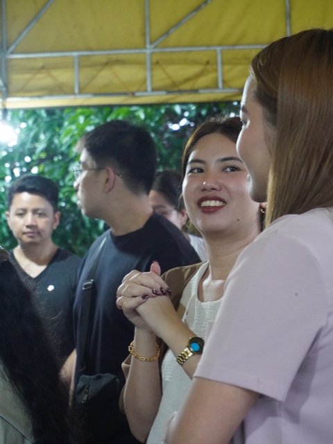 A smiling young woman holds hands with a friend in a crowd under a tent