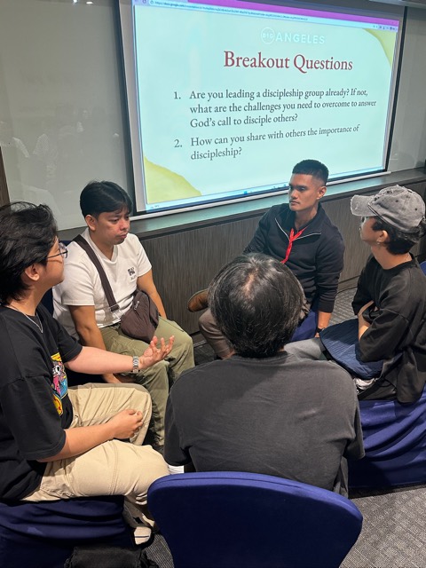 A small group of men in a breakout discussion circle under the breakout questions slide